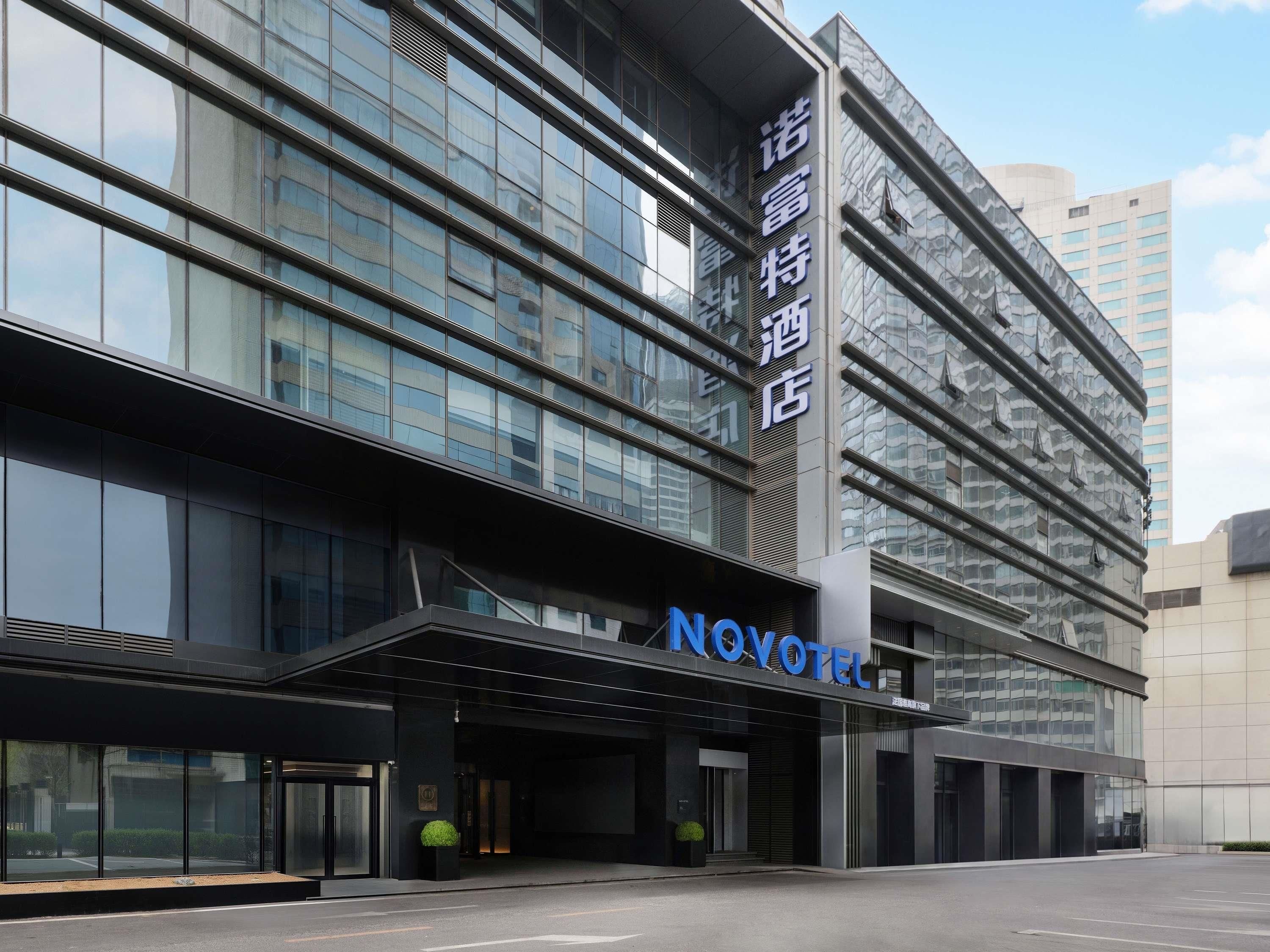 Un hotel moderno con fachada de vidrio, un llamativo letrero de 'NOVOTEL' y un cartel vertical con caracteres chinos.