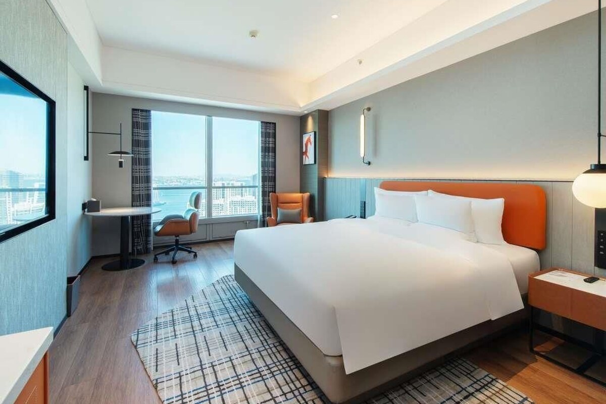 Ein modernes Hotelzimmer mit einem großen Bett, einem Schreibtisch, einem Stuhl und Blick auf die Stadt.