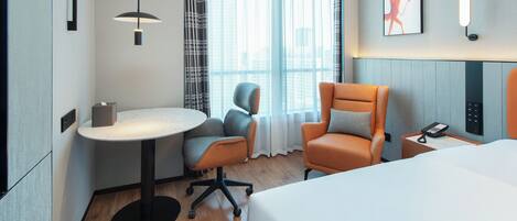 Habitación de hotel con cama, escritorio con silla, una mesita, teléfono y ventana con cortinas.