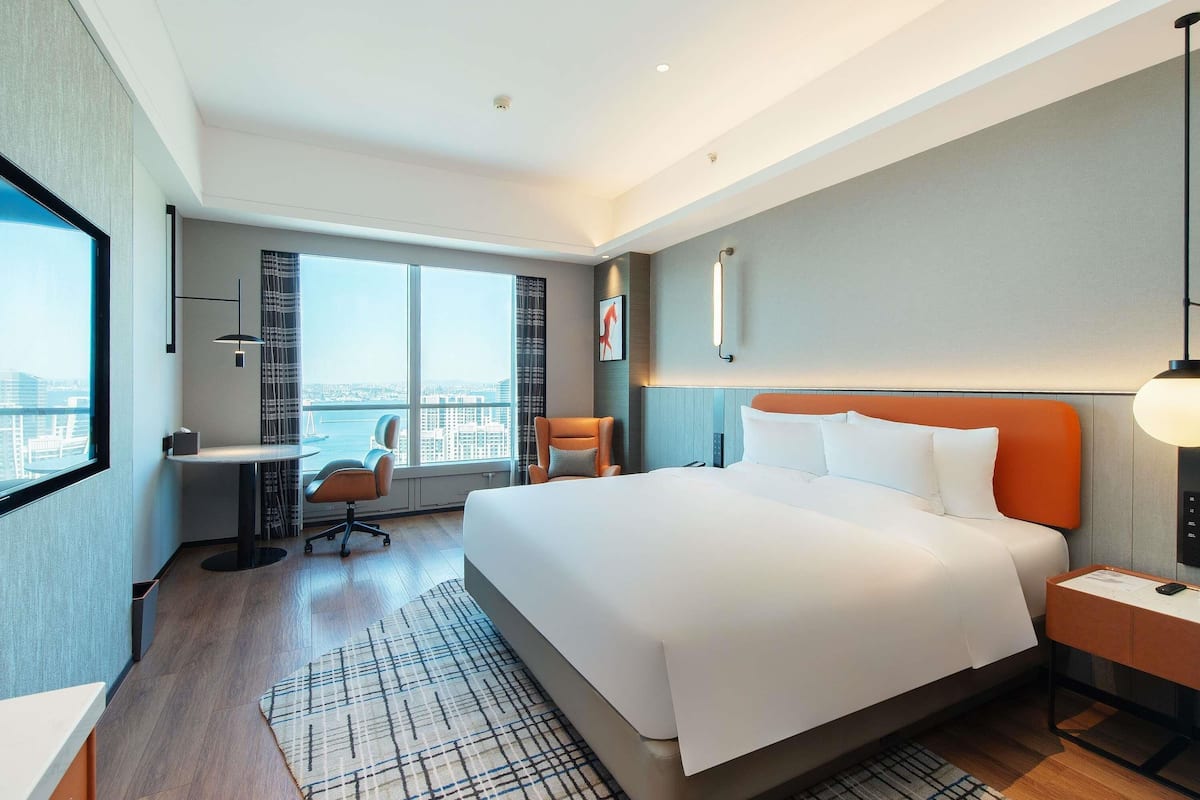 Habitación de hotel moderna con una cama grande, un escritorio, una silla y vistas a la ciudad.