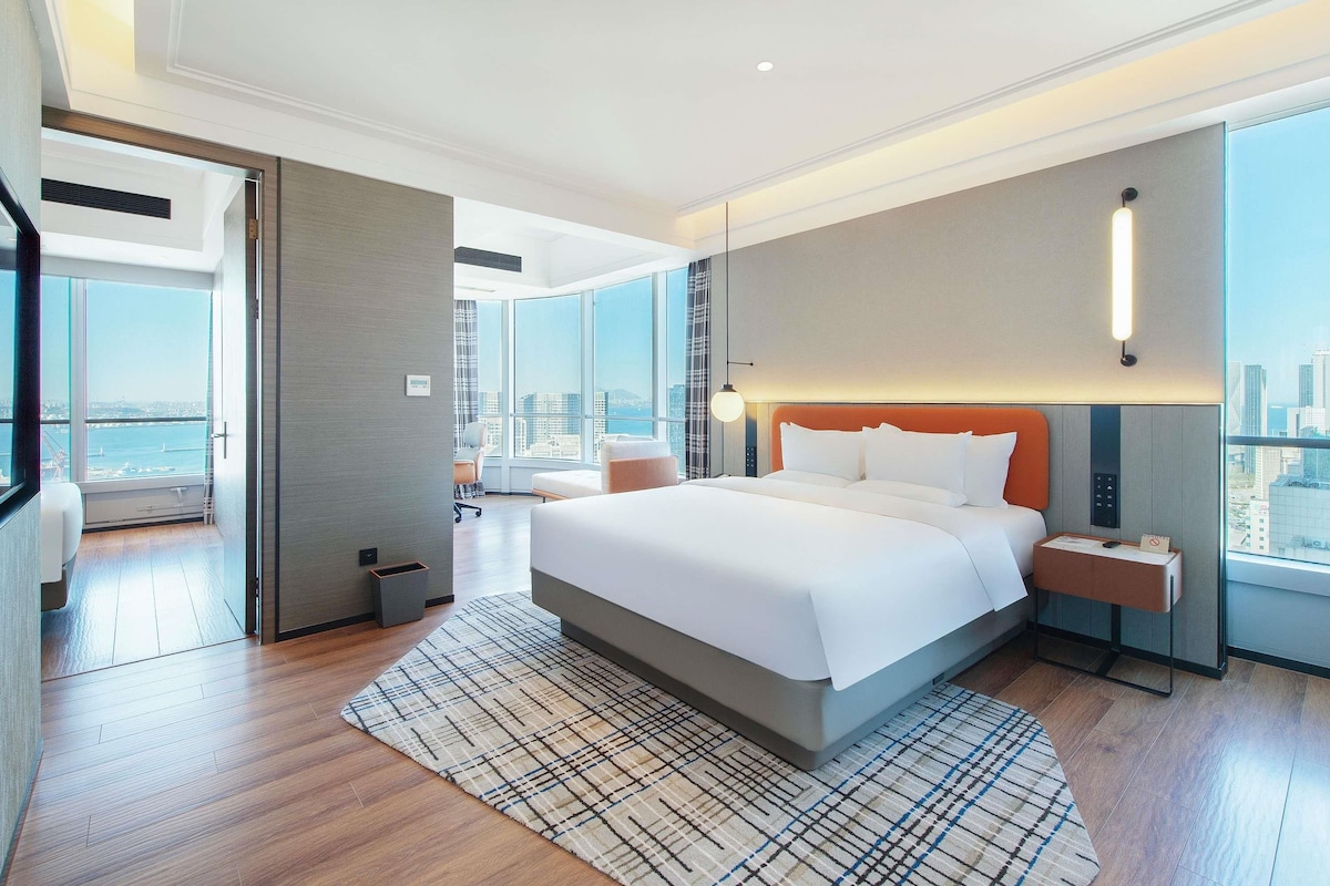 Een moderne hotelkamer met een groot bed, stadszicht, een bureau en een stoel.