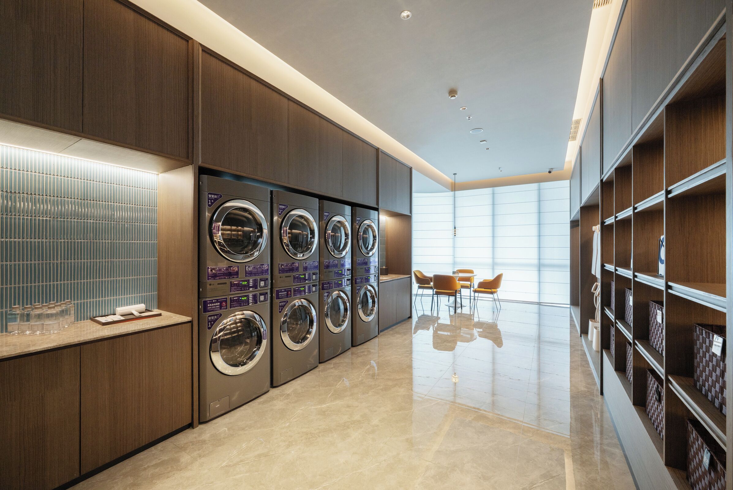 A modern laundry facility with multiple washing machines, a tiled wall, and a clean, polished floor.