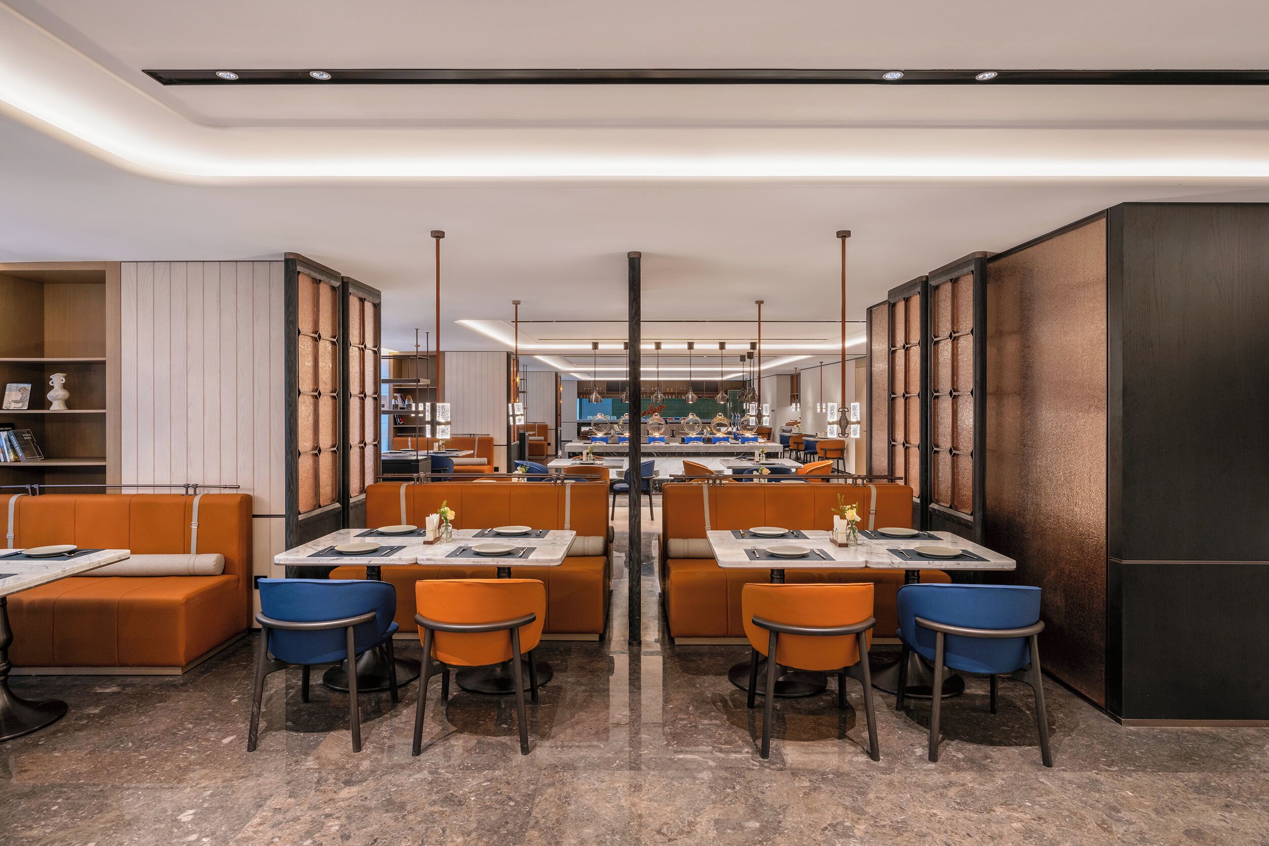A modern restaurant with high tables and orange booths, featuring a central island and pendant lighting.