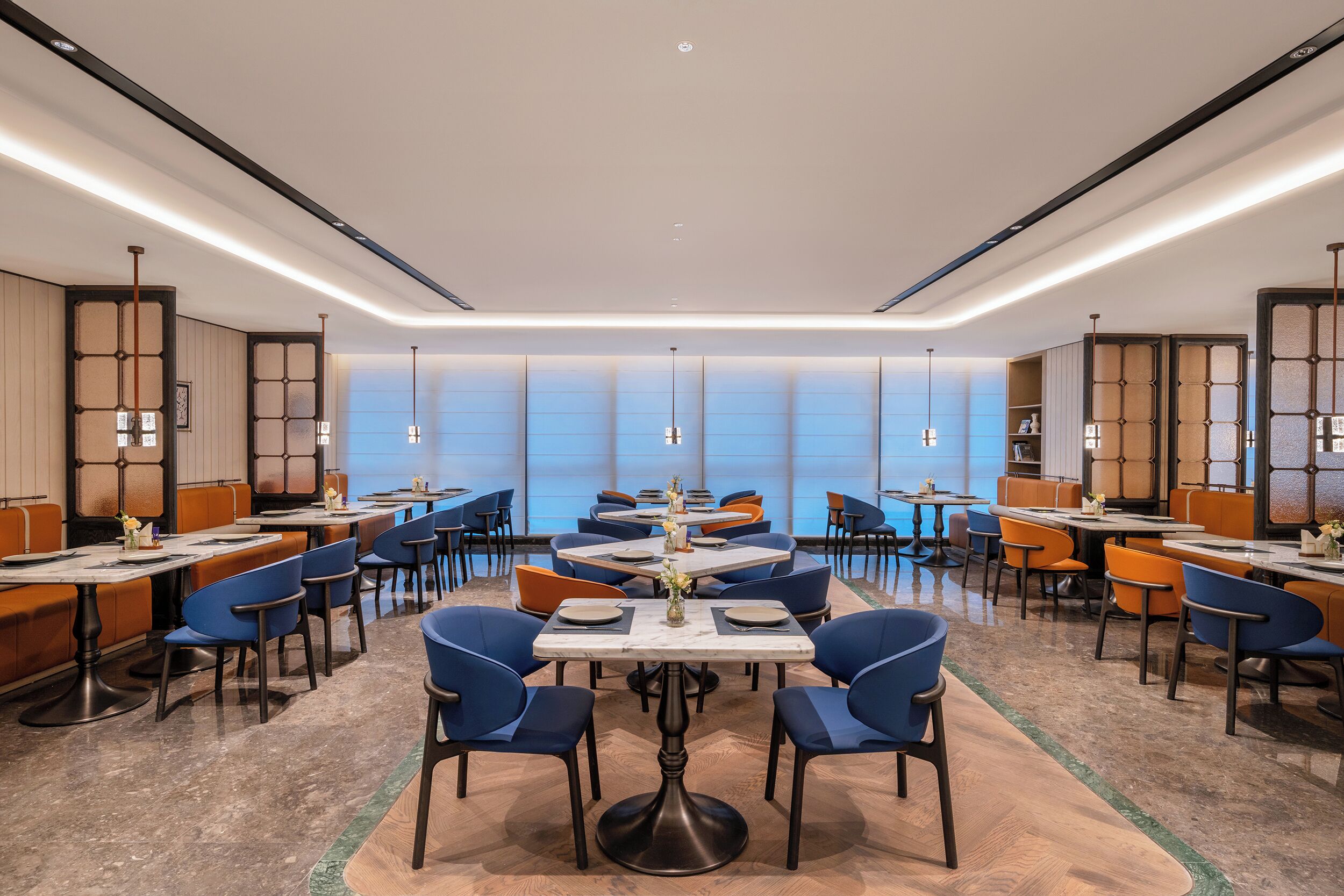 Un comedor moderno con mesas y sillas, una pieza decorativa central, y vistas a través de amplios ventanales.