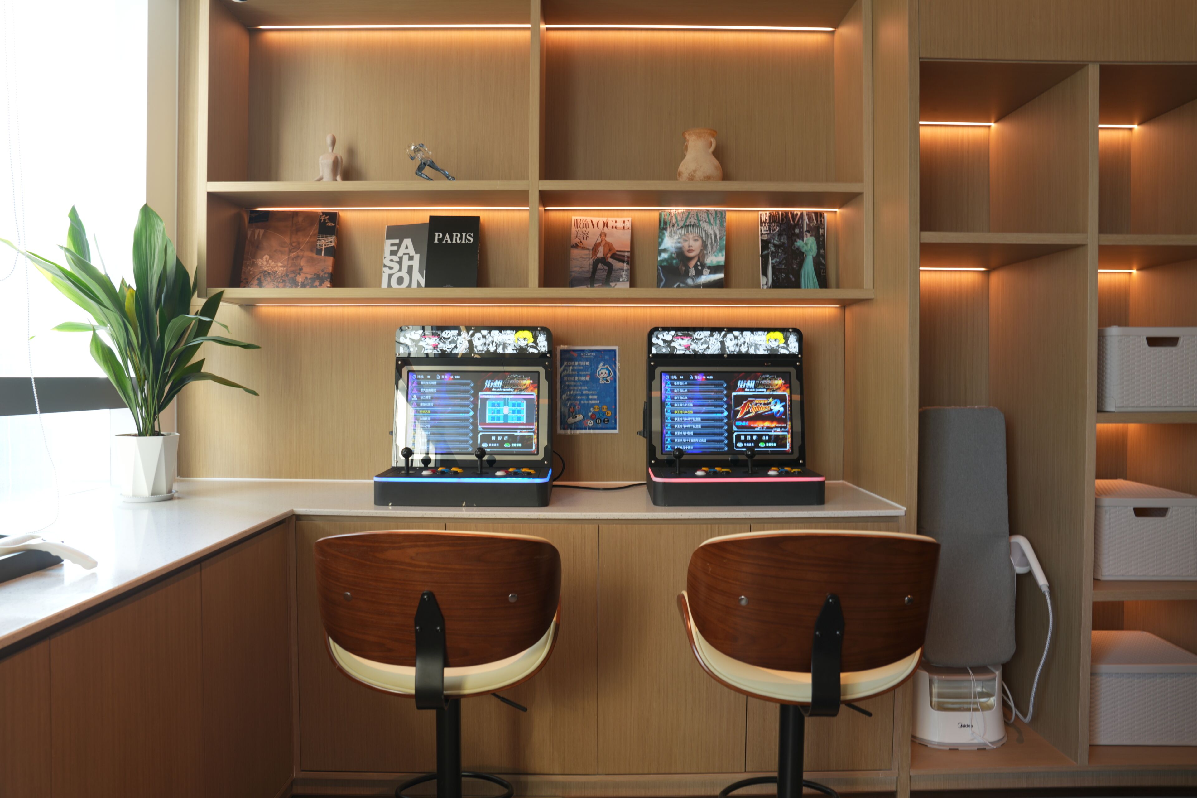 Un área de bar moderna con dos taburetes, una planta en maceta y estantes con libros y objetos decorativos.