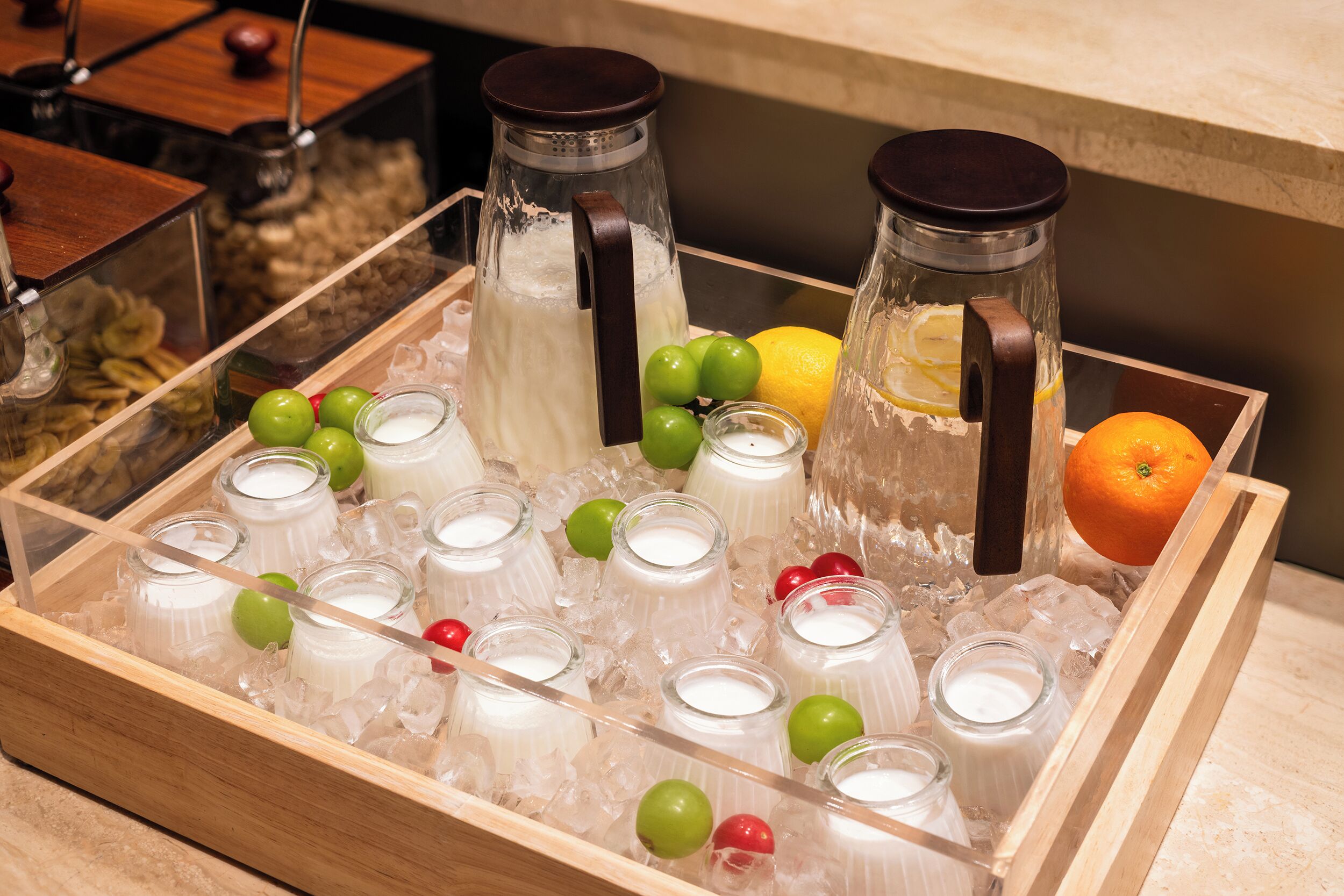 A tray of milkshakes with ice, lemons, and oranges on a wooden surface.