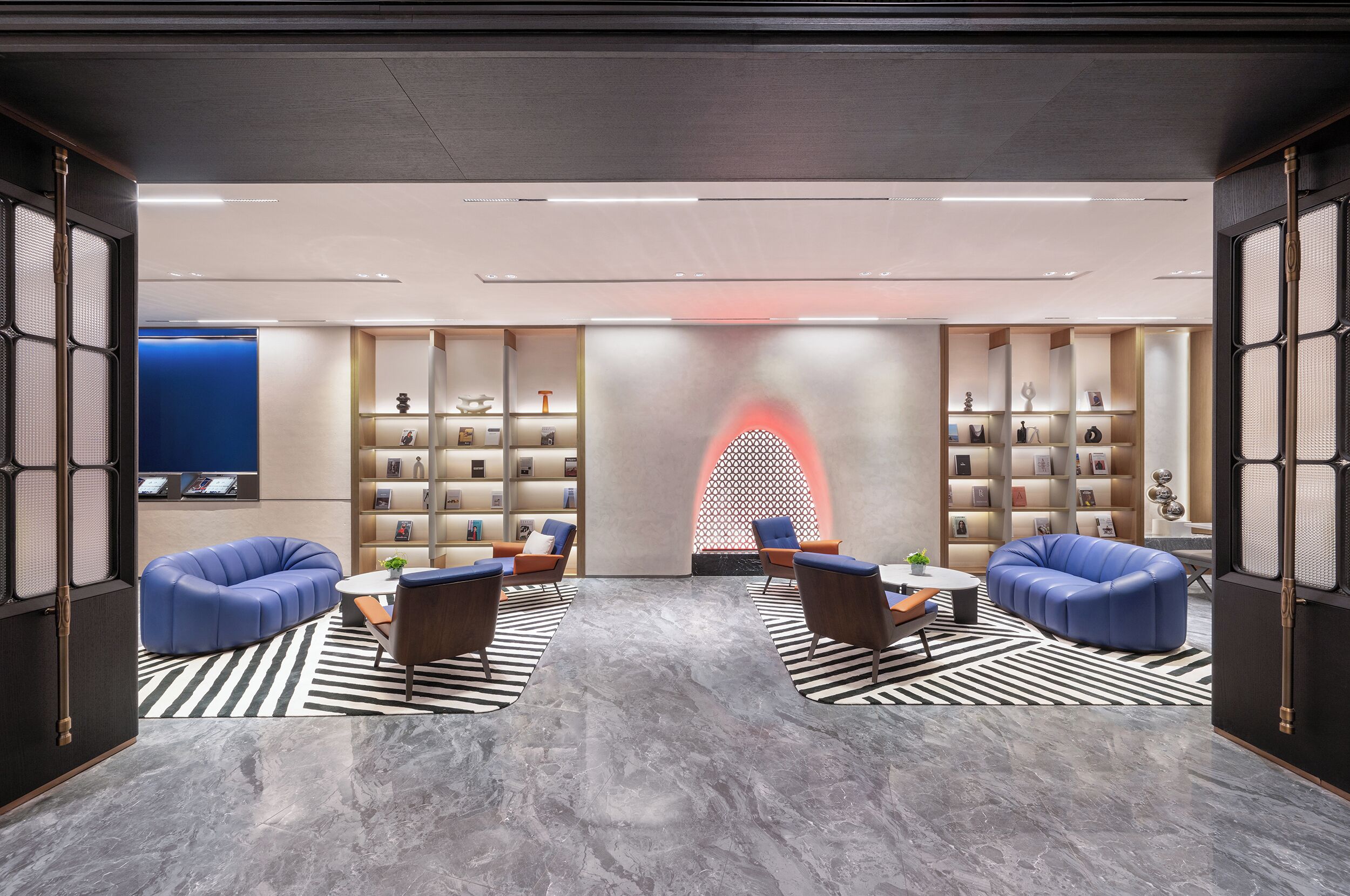 A modern lobby with a central seating area, a patterned floor, and a wall with shelves containing various items.