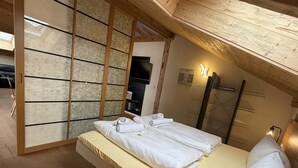 A bedroom with a wooden slat partition, a bed with neatly folded towels, and a shelf with books. - Vacation apartment Haus Bader (Garmisch-Partenkirchen)