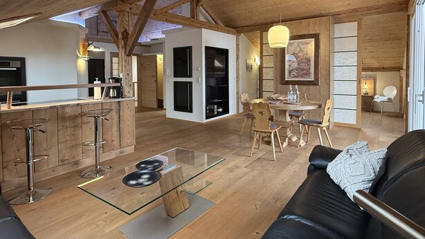 A spacious loft with a high ceiling, a dining area, a kitchen, and a living room with a glass coffee table. - Vacation apartment Haus Bader (Garmisch-Partenkirchen)