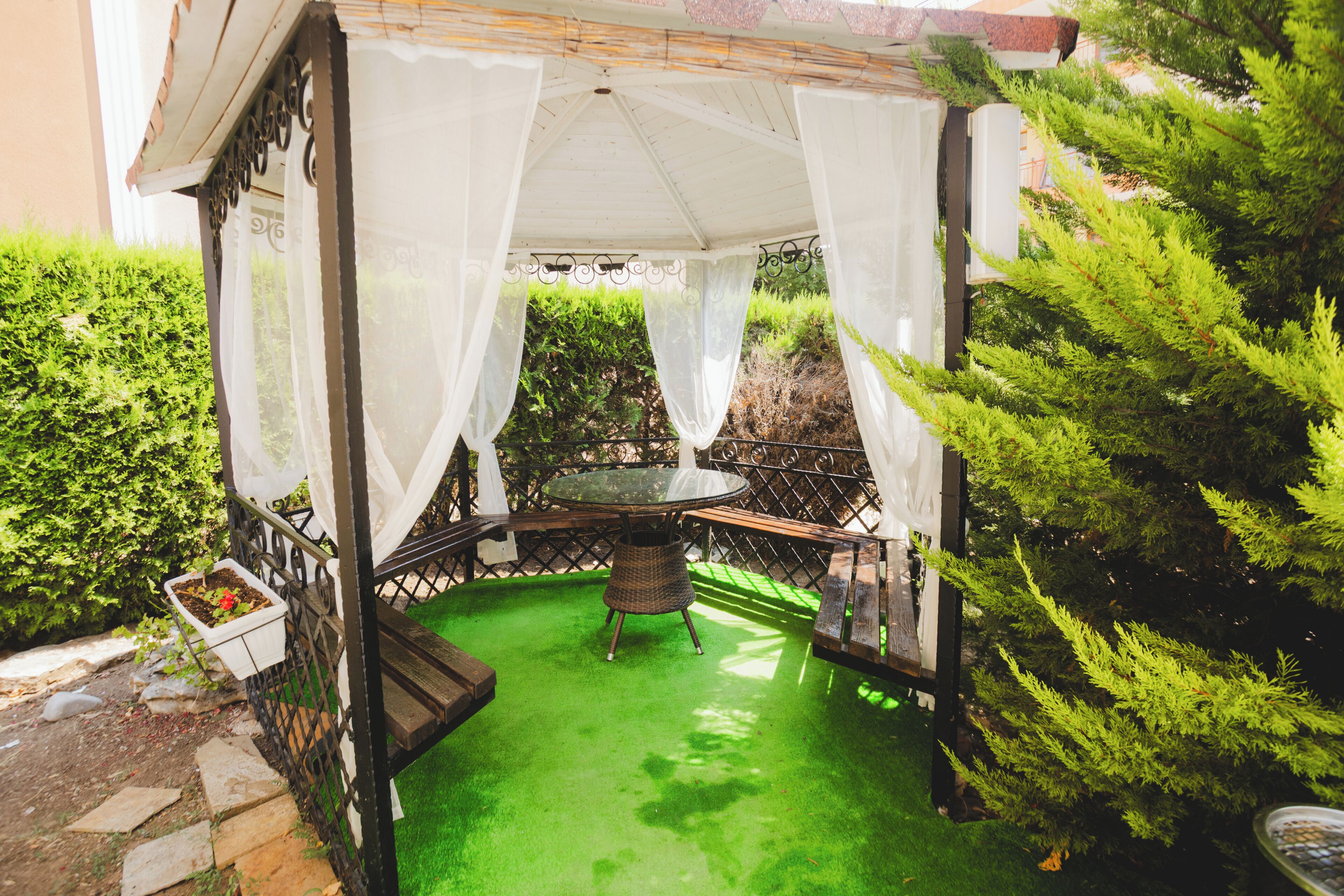 Un espace extérieur abrité, aménagé avec une table et des chaises, entouré de verdure et d’une haie.