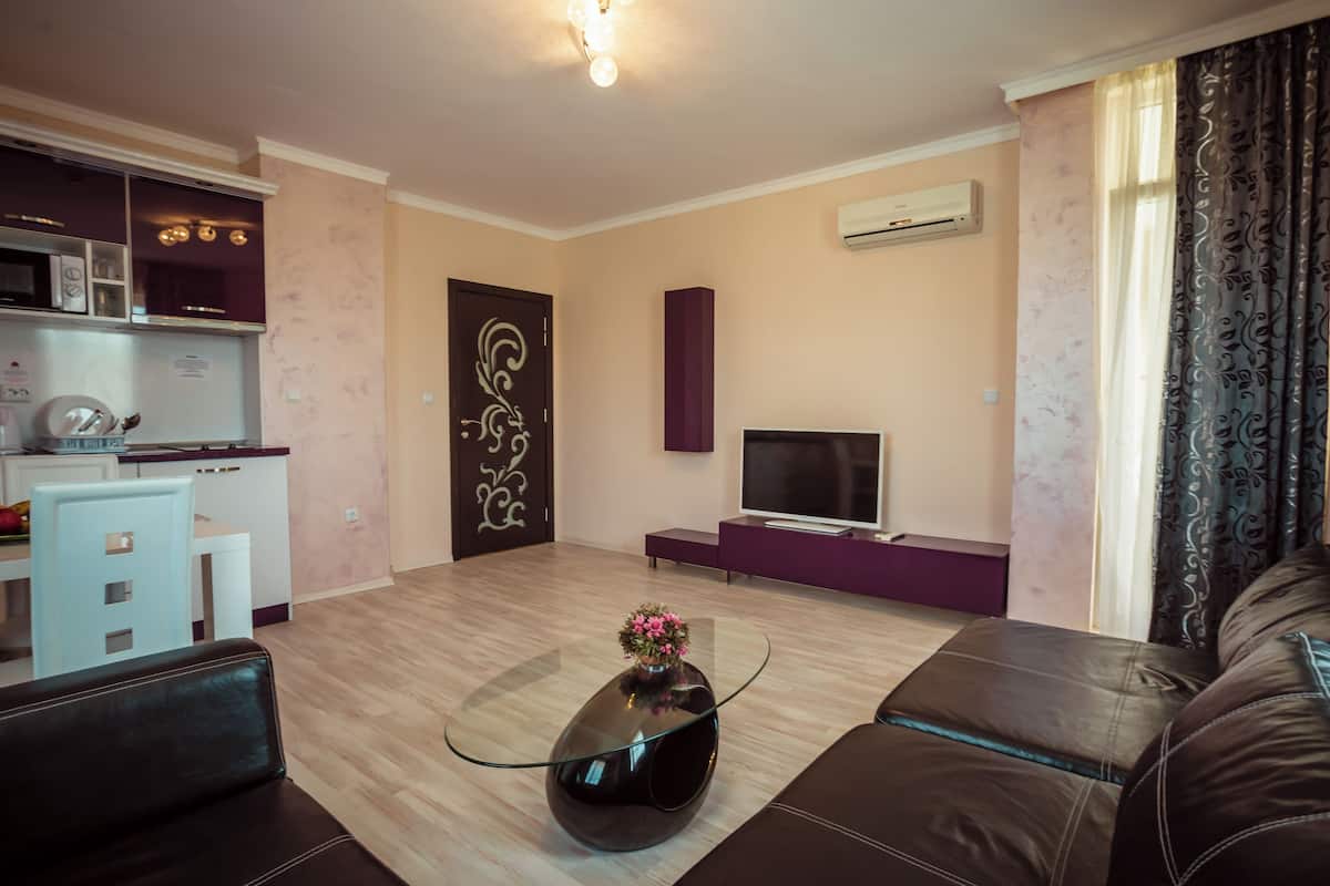A living room with a sofa, a coffee table with a flower vase, a TV, a kitchen area with a microwave, and a decorative door.