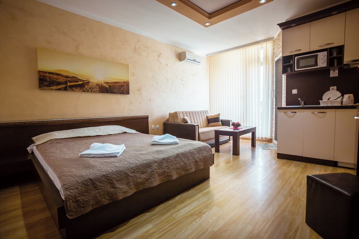 A hotel room with a bed, a sofa, a small table, a microwave, and a painting on the wall.