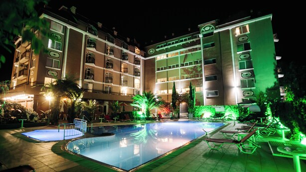 Een hotel met een zwembad, terras en een goed verlichte gevel.