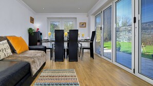 Ein Wohnzimmer mit einer Couch, einem Esstisch mit Stühlen und großen Schiebeglastüren zum Außenbereich.