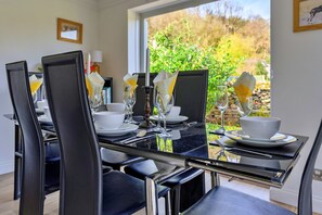 A dining table with chairs, a candle, and a view of greenery outside. - Dyffryn (Betws-Y-Coed)