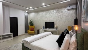 A modern bedroom with a large bed, a desk, a TV, and a chair. - Goshen Trust Hotel And Suites (Idanre)