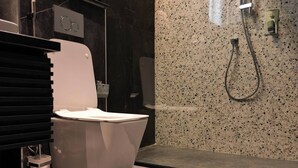 A modern bathroom with a white toilet, a black vanity, and a shower area. - Goshen Trust Hotel And Suites (Idanre)
