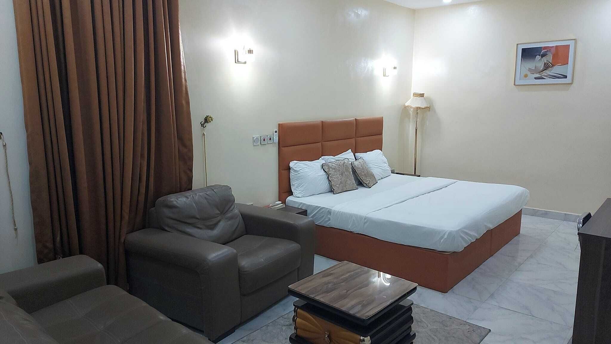 A bedroom with a bed, a chair, a bedside table, and a lamp.