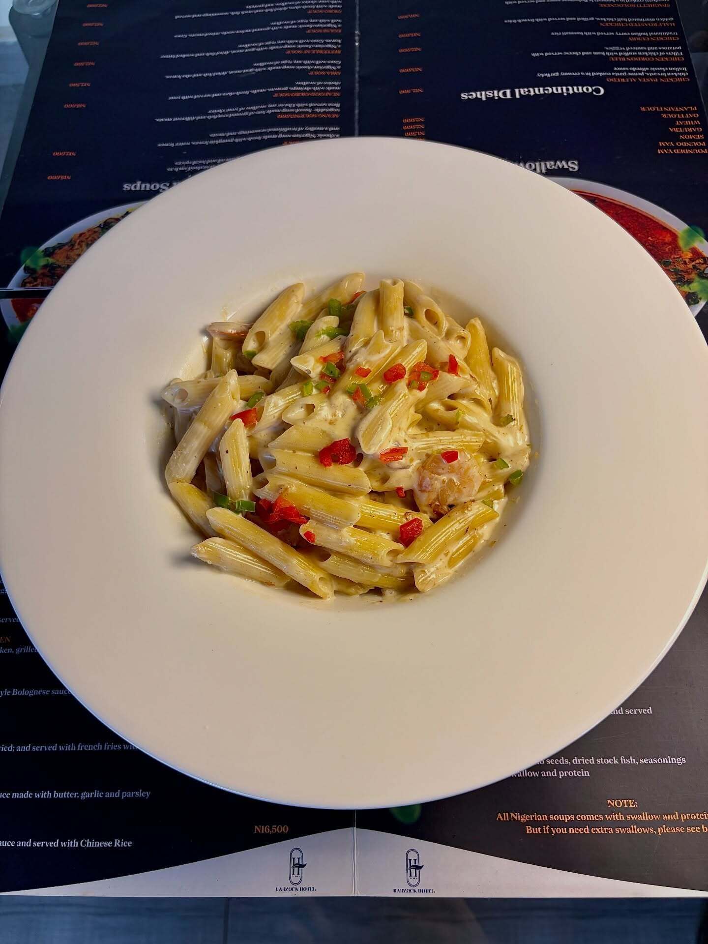 Un plato blanco de pasta con verduras sobre una mesa con un menú.