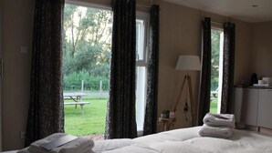 A hotel room with a bed, a desk, a lamp, and a view of a garden. - Hotel De Brabantse Biesbosch (Werkendam)