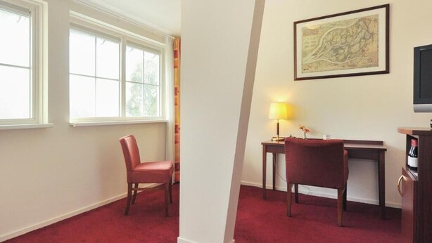 A room with a red carpet, a desk with a lamp, a chair, and a map on the wall. - Hotel De Brabantse Biesbosch (Werkendam)