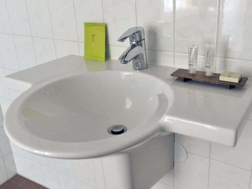 A bathroom with a white sink, chrome faucet, and a small shelf with toiletries.