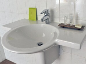 A bathroom with a white sink, chrome faucet, and a small shelf with toiletries.