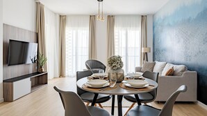 A modern living room with a dining area, a sofa, a TV, and a large window with curtains. - A60 Boutique Hotel (Budapest)