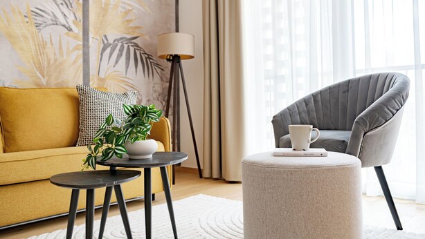 A modern living room with a sofa, a round table, a grey armchair, a floor lamp, and a large window with curtains. - A60 Boutique Hotel (Budapest)