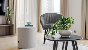 A modern living room with a round table, a grey armchair, a potted plant, and a small ottoman with a book and cup. - A60 Boutique Hotel (Budapest)