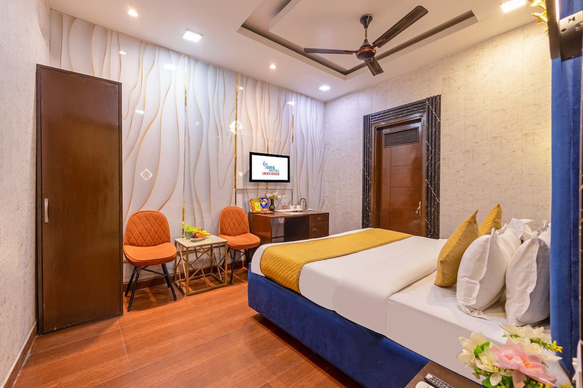 A hotel room with a bed, desk, chairs, a television, and a ceiling fan.
