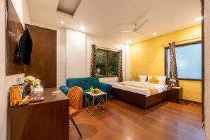 Habitación de hotel con cama, sofá, escritorio con aperitivos, silla y ventana con cortinas.