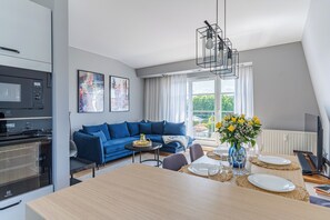 A modern living room with a blue sofa, a dining table set for four, and a kitchen area with a microwave and oven. - Imperial Apartments - Sopocki Parkur (Sopot)