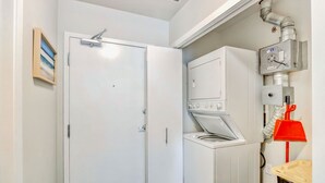 Un cuarto de lavado con lavadora y secadora blancos, un recogedor rojo y un sistema de ventilación.