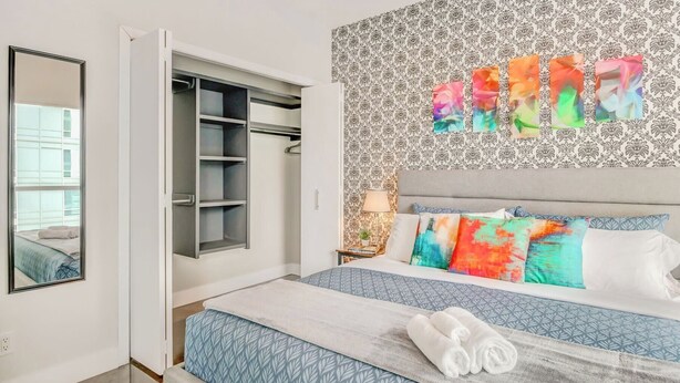 Un dormitorio con una cama, un armario, un espejo y un papel tapiz estampado.