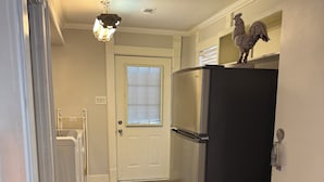 Un pasillo estrecho con piso de madera, una puerta blanca con ventana, un refrigerador de acero inoxidable y un ventilador de techo.