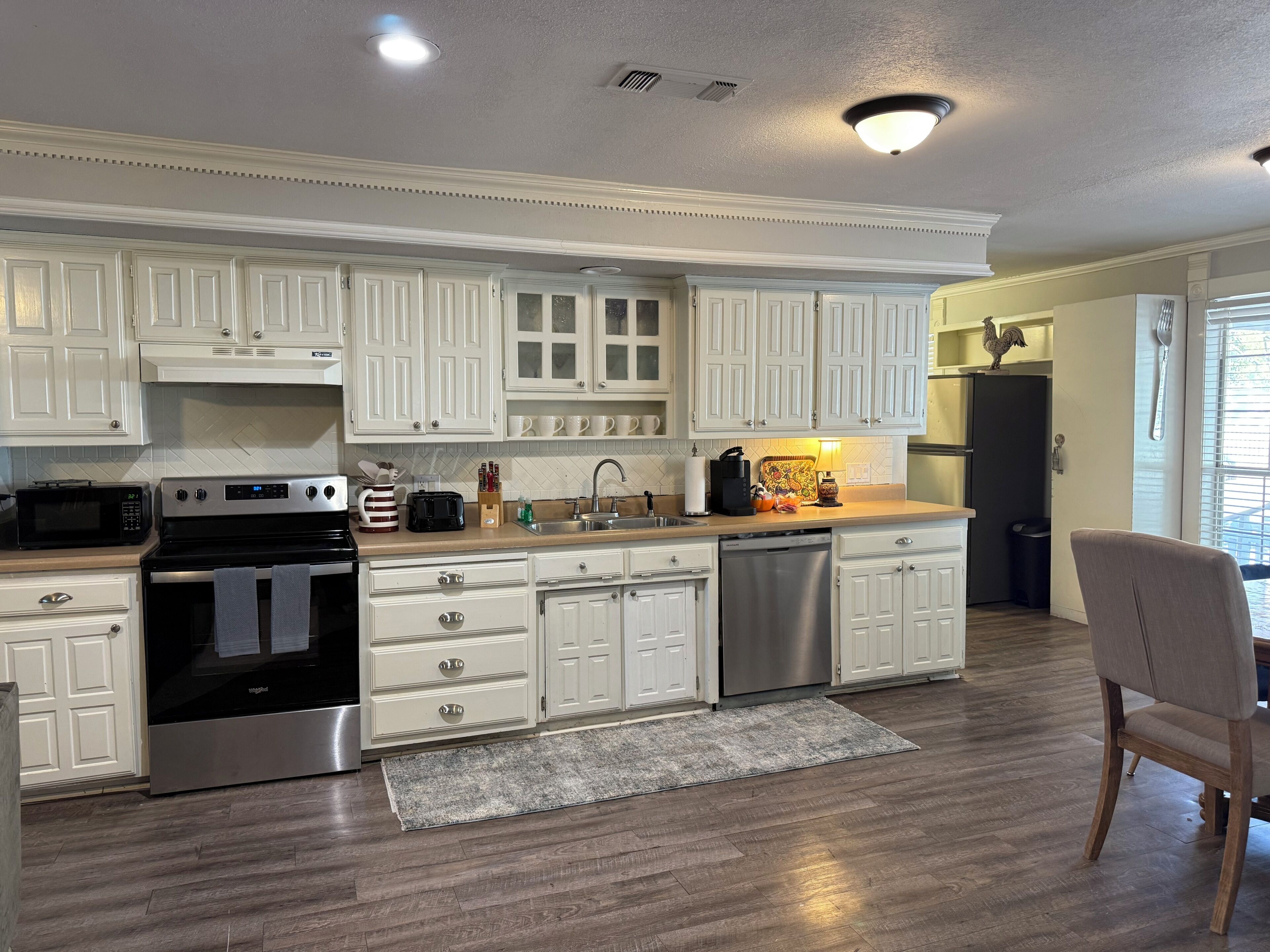 A modern kitchen with white cabinetry, stainless steel appliances, and a wooden floor.