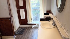 Un baño con tocador de madera, un espejo grande, una ventana y una zona de ducha.