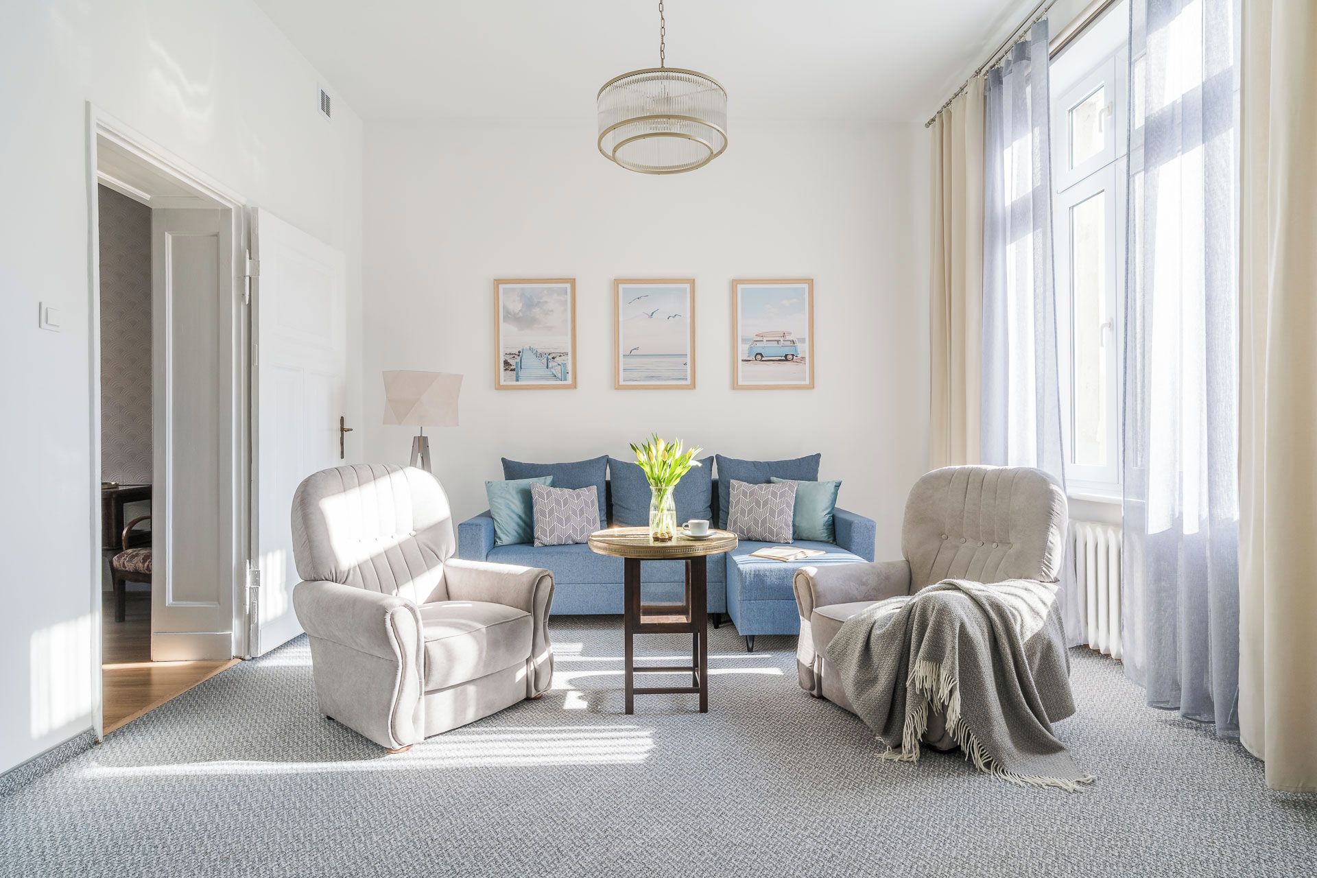 Un salon comprenant un canapé, deux fauteuils, une table basse avec un vase, et trois tableaux encadrés accrochés au mur.