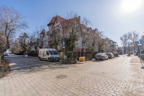 Eine gepflasterte Straße mit parkenden Autos, einem Lieferwagen und einem Gebäude mit rotem Dach.