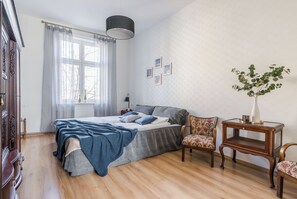 Ein Schlafzimmer mit Bett, Stuhl, Tisch und einem Fenster mit Vorhängen.