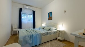 Een slaapkamer met een bed, nachtkastjes, een stoel, een raam met gordijnen en een schilderij aan de muur.