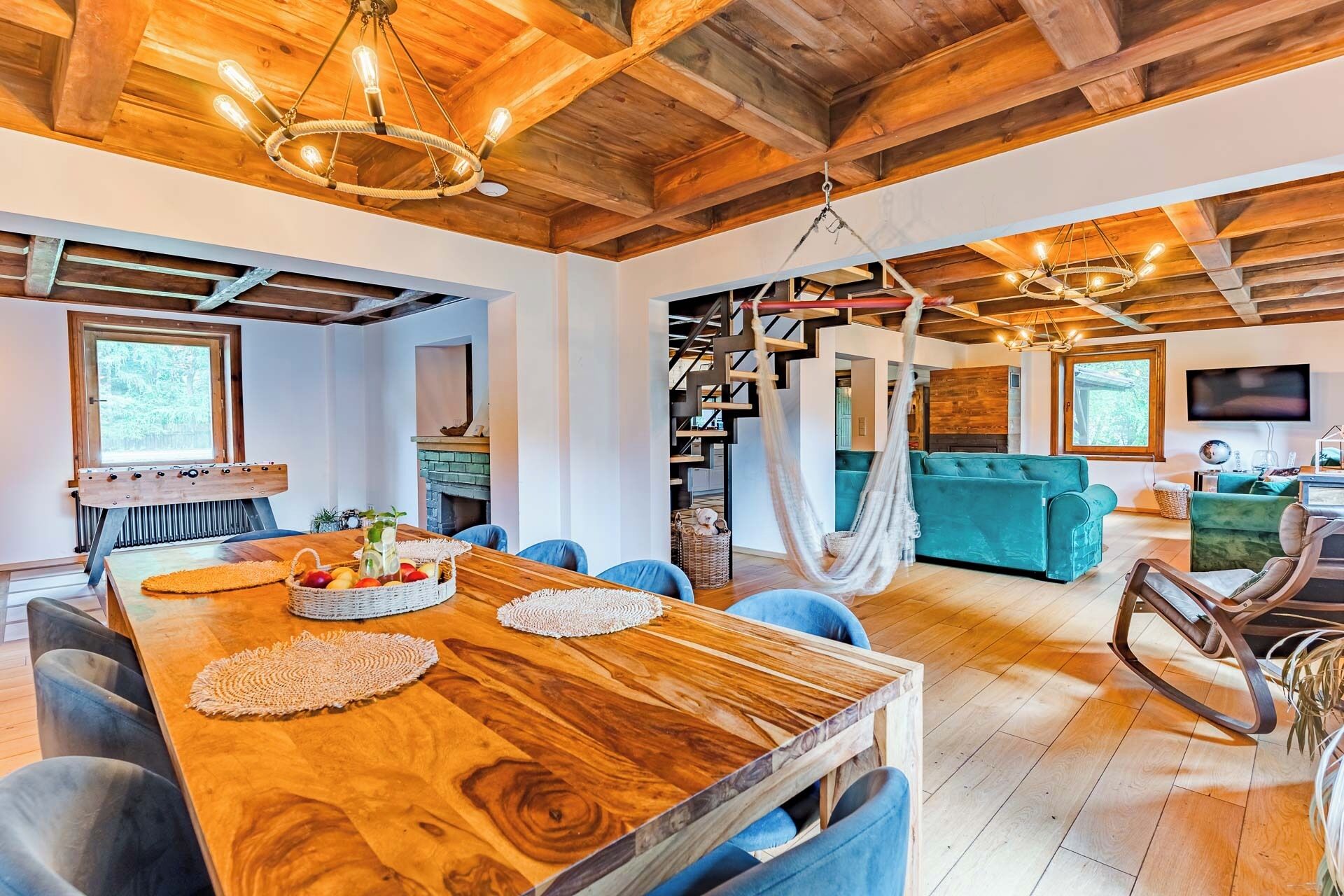A spacious living area with a wooden ceiling, a dining table with a fruit basket, a sofa, and a TV.