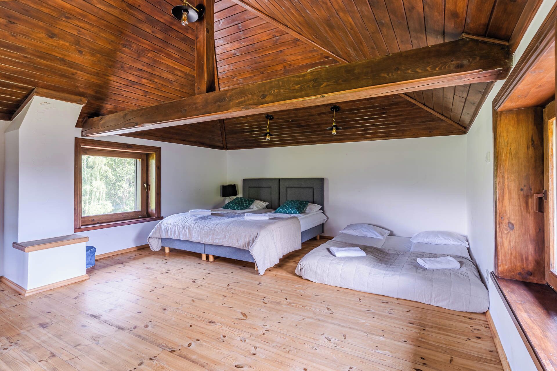 A room with wooden floors, a large window, and a bed with two pillows.
