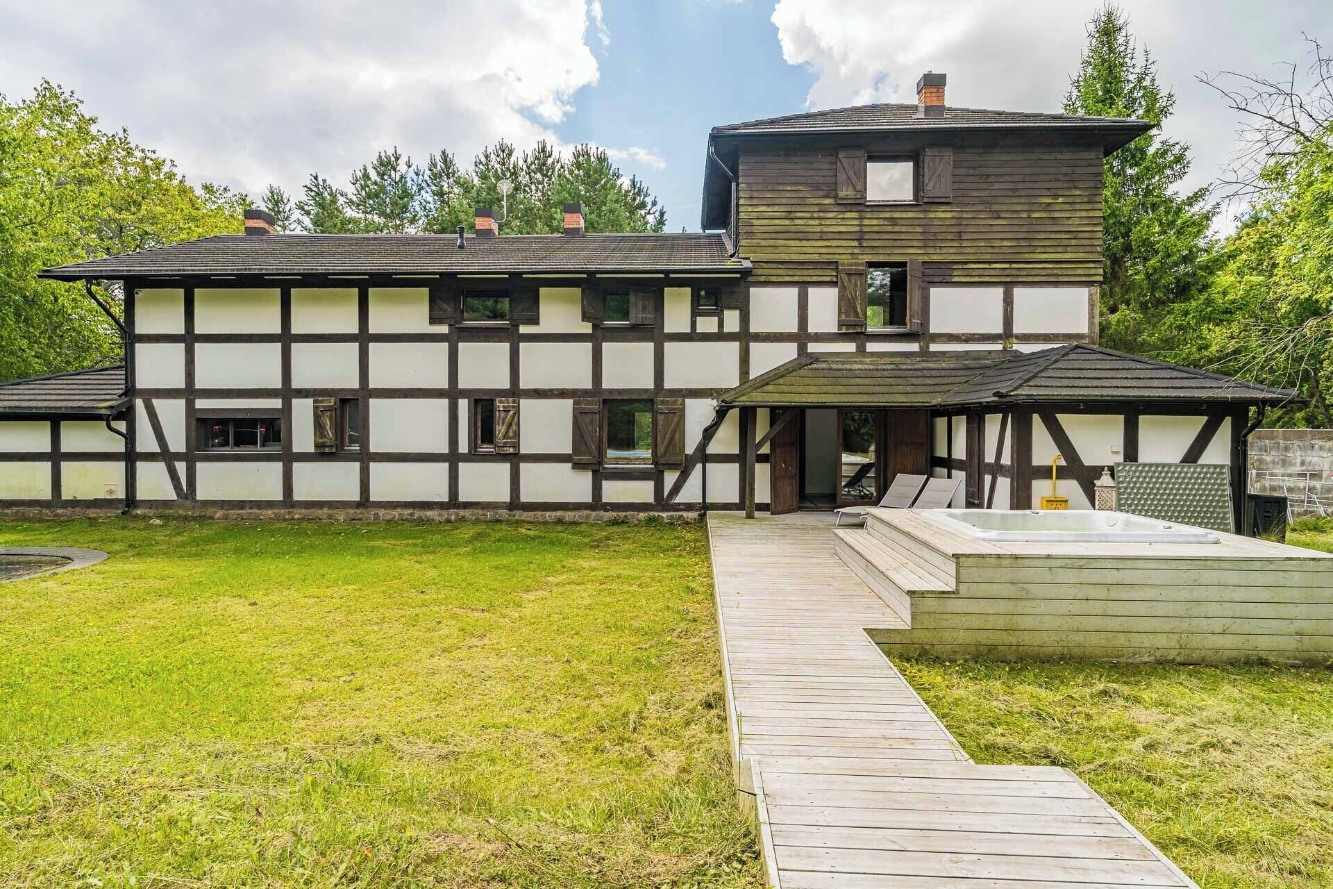A two-story building with a wooden exterior, a covered porch, and a small outdoor hot tub area.