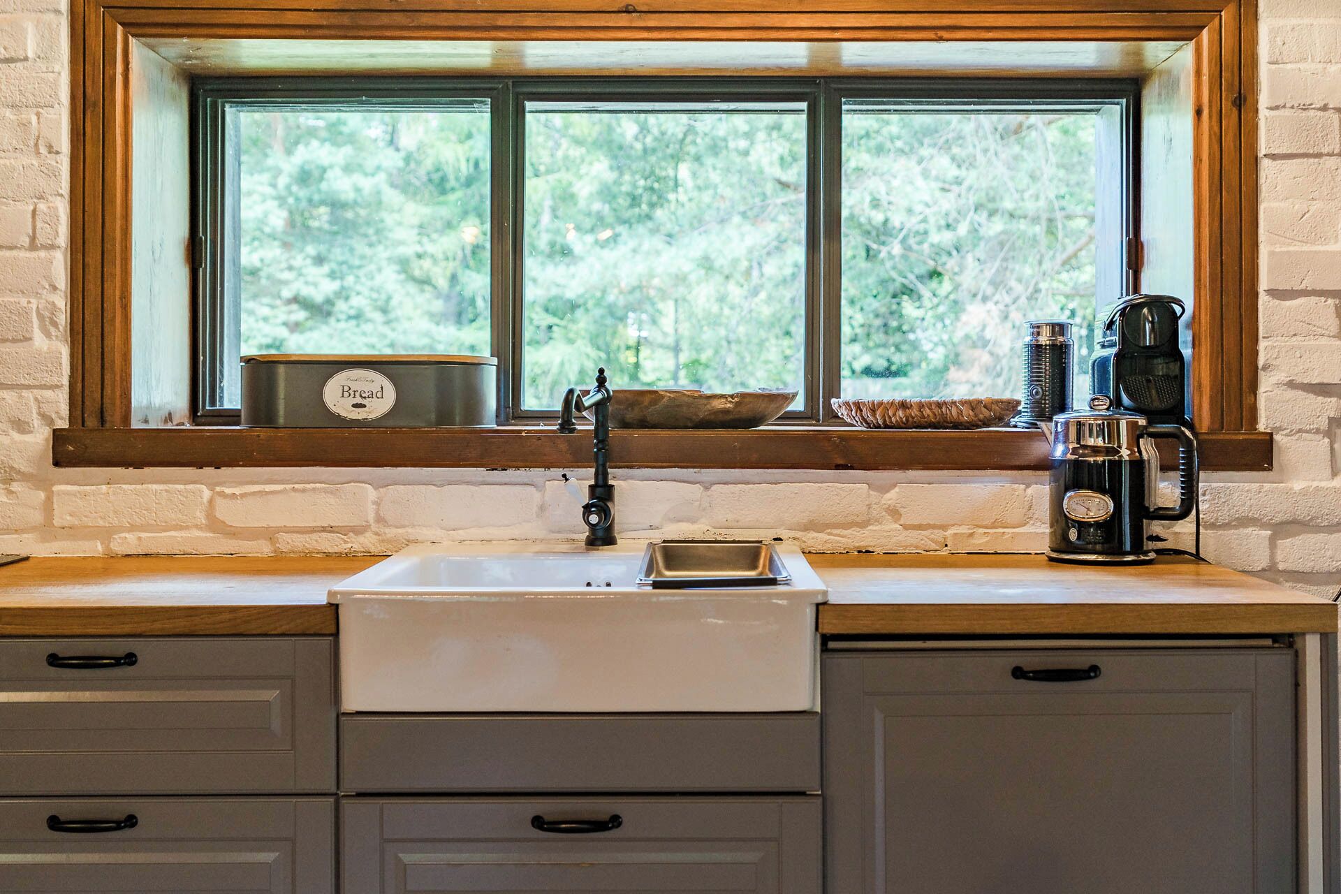 Una cocina con ventana, un lavamanos, una panera y una cafetera.