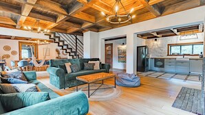 Un amplio salón con un conjunto de sofás, una mesa de centro y un comedor con sillas. Una escalera conduce a otro nivel, y se ve una cocina al fondo.