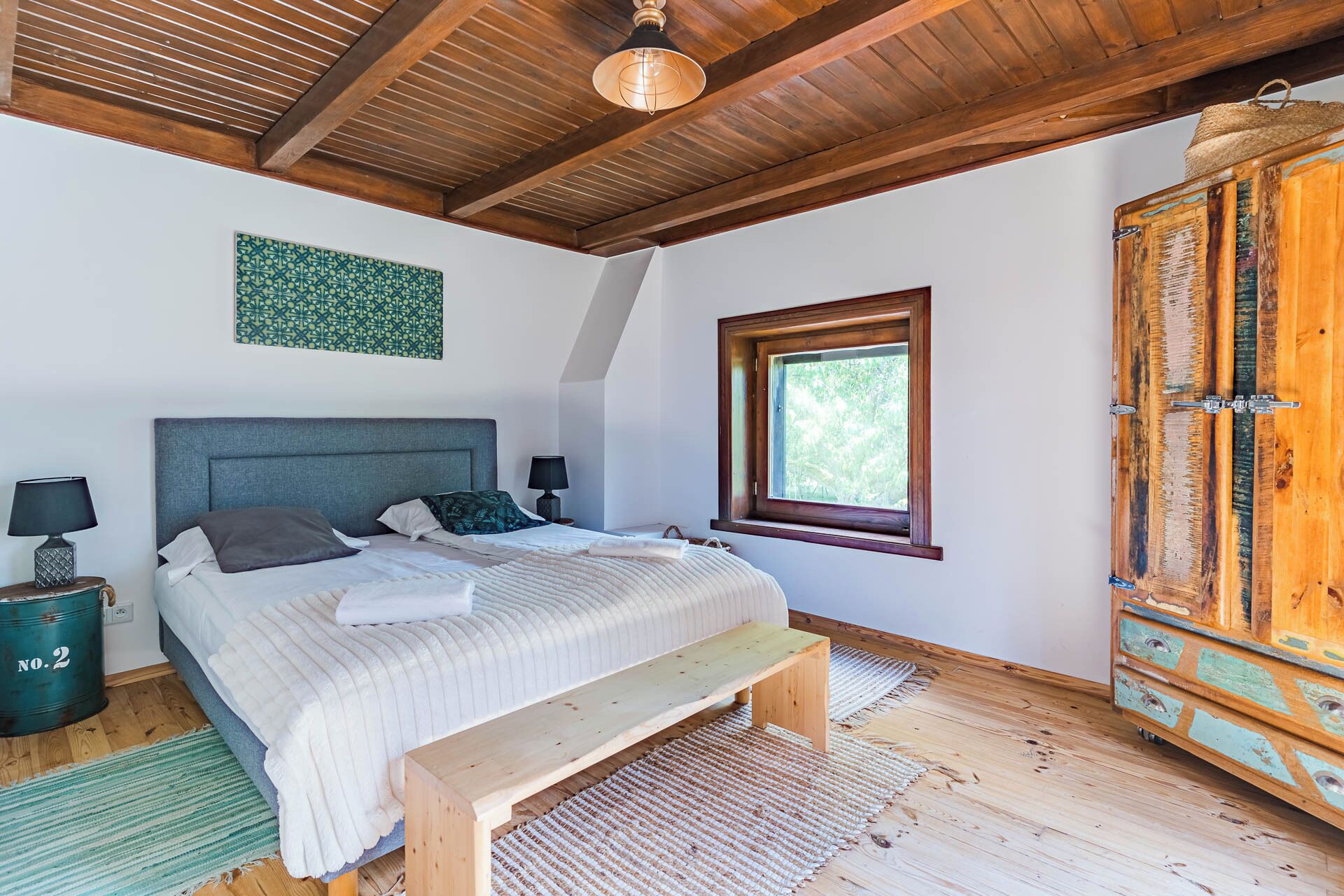 Une chambre à coucher avec un lit, des lampes de chevet, un banc, une fenêtre et une armoire en bois.