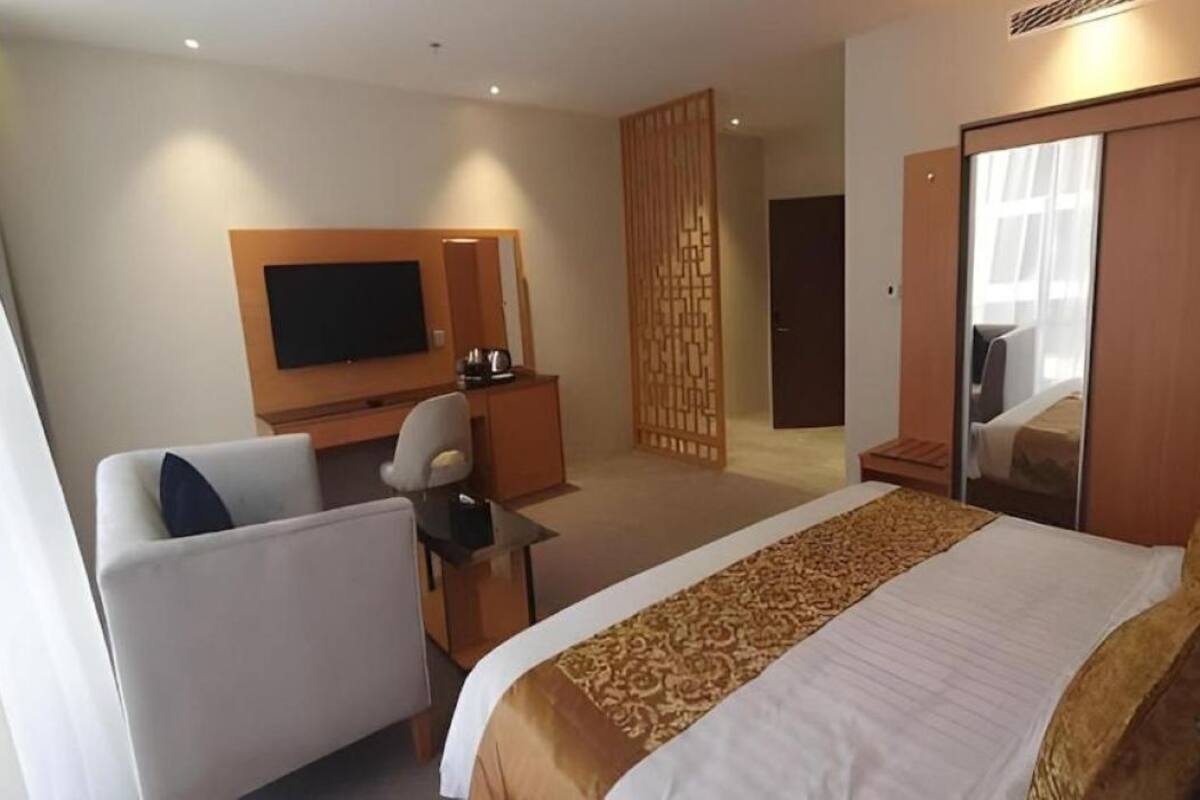A hotel room with a bed, a desk, a chair, a TV, and a wardrobe.