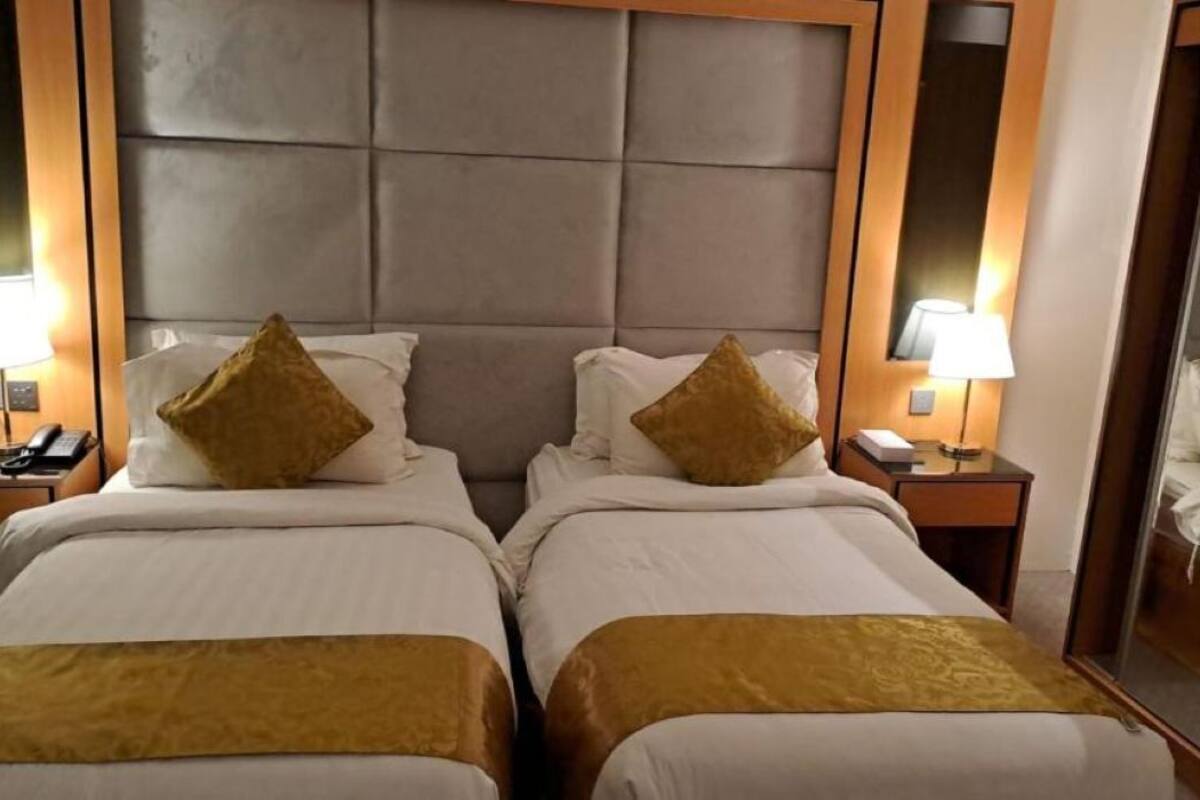 A hotel room with two beds, a padded headboard, bedside lamps, and a mirror.